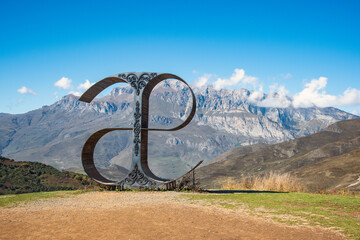 Fototapeta premium A tourist place is an art object of the letter of the Ossetian alphabet against the background of mountains and blue sky. North Ossetia-Alania