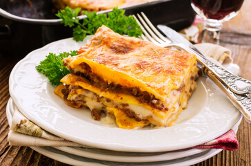 Traditional Italian lasagne with ground meat and bechamel sauce served as close-up with red wine on a classic design plate