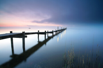 Obraz premium long wooden pier over the calm sea, tranquil morning with beautiful sunrise, peaceful and quiet