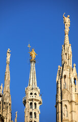 golden statue of Virgin Mary and blue sky in background in Milan Cathedral in Italy