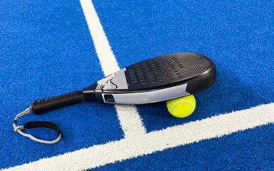 Black professional paddle tennis racket and ball on blue background. Horizontal sport theme poster,...