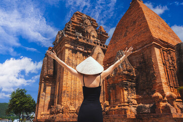 A female tourist in a traditional Vietnamese conical head on the background of Cham Towers.