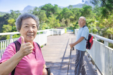 Happy asian senior couple hiking in the nature and showing thumbs up