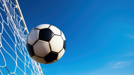 Fototapeta premium A soccer ball captured mid-motion against a clear blue sky, just as it meets the net, symbolizing energy and triumph.