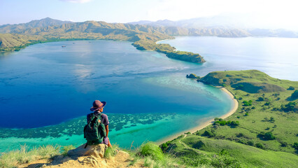 A man sits on a rock against the backdrop of mountains and the sea at Gili Lawa, Komodo National Park, Indonesia. summer background and summer holiday concept.  © Balnyes Visuals