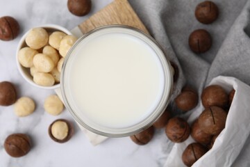 Glass of macadamia milk and nuts on white marble table, flat lay