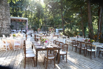 A charming outdoor wedding reception with long wooden tables adorned with floral arrangements, set against a backdrop of lush greenery and a stone wall