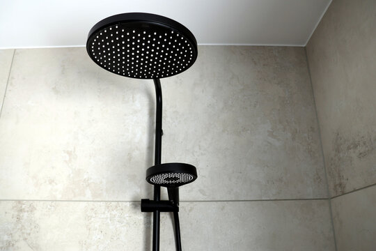 Mattschwarzes Regenduschsystem mit gro&szlig;er Kopfbrause und Handbrause vor grauen Wandfliesen in einem modern renovierten Badezimmer.