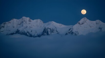 Snow-capped mountain peaks above the clouds under the moonlight on a full moon. Mountain peaks above the clouds under the moon at night.