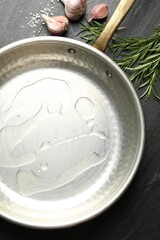 Frying pan with cooking oil, rosemary, garlic and salt on dark textured table, flat lay