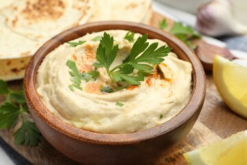 Delicious hummus with parsley, paprika, pita and lemon on table, closeup