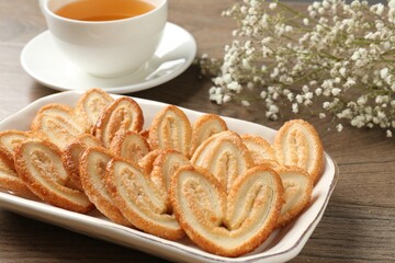 Tasty french palmier cookies, tea and gypsophila flowers on wooden table, closeup