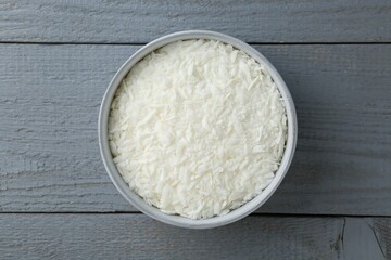 Soy wax in bowl on grey wooden table, top view