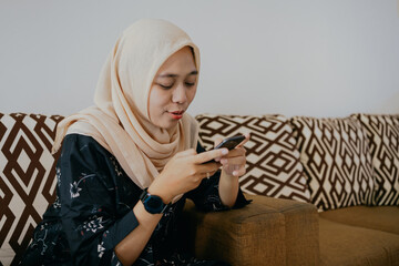 Millennial modern lifestyle concept.
Asian woman in hijab using mobile phone sitting on sofa in office.