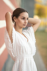 Portrait of a young beautiful girl in a white dress outdoors in an urban environment.