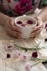 Female hands holding a cup of cappuccino with flowers on a book background