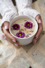 Female hands holding a cup of cappuccino with flowers on a book background