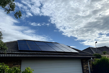 A house featuring solar panels on the roof under a partly cloudy sky.