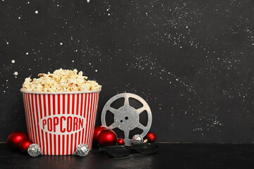 Composition with film reel, big bucket of popcorn and Christmas decorations on table against black...