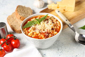 Bowl of pasta fagioli with cheese, basil and tomatoes on white background