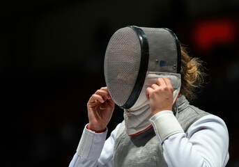 Fencer preparing for a match in a competitive arena, adjusting protective gear during a sporting event at a national tournament