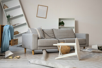 Interior of messy living room with sofa, shelf units and overturned table after earthquake