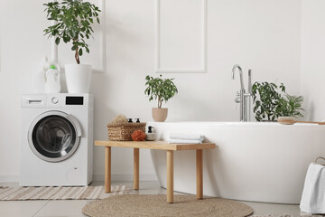 Interior of light bathroom with bathtub, houseplants and wooden bench