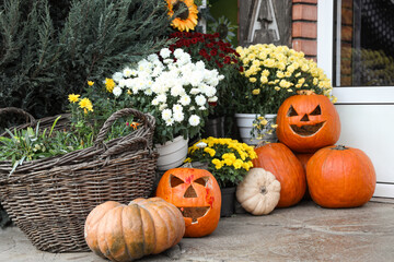 Wicker basket with bouquets of autumn flowers and Halloween pumpkins on ground outdoors