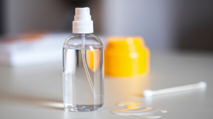 Promotional photo of a bottle with micellar spray water on the table. A bright yellow cream and a cotton swab are depicted in the background. With a place for the text.
