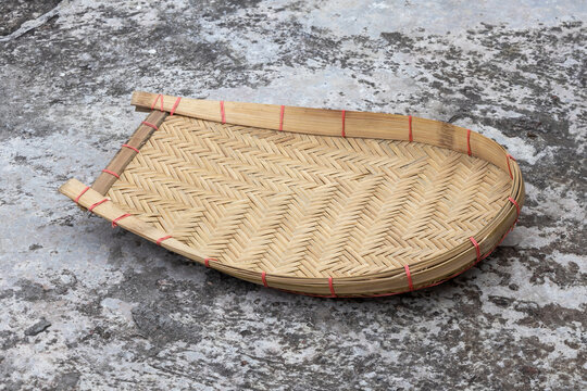 A Kula or Kulo, bamboo cane made winnowing fan, placed on concrete floor. This traditional tool is essential for Bangladeshi farmers to separate grain from chaff by tossing it in the air.