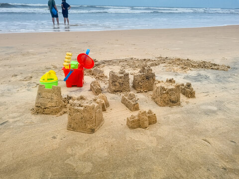 Children's play area on beach with multiple sand castels, colorful toys buckets, shovel, with people in distance showing skill development and infrastructre planning