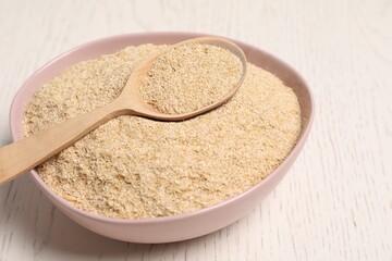 Oat bran in bowl and spoon on light wooden table, closeup