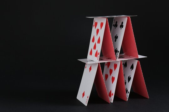 House of playing cards on black background, space for text