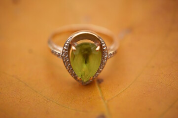 A precious ring with chrysolite on the background of an autumn leaf.