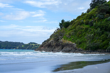 Serene Coastal Landscape Featuring Gentle Waves Lapping Against Rocky Shoreline Surrounded by Lush Green Hills and Clear Blue Sky