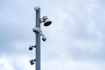Surveillance Cameras and Speakers Installed on a Metallic Pole Against a Cloudy Sky, Representing...