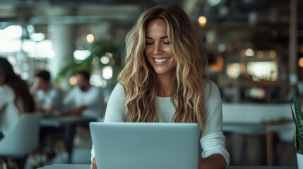 Fototapeta premium A cheerful young woman sitting in a bright workspace, engaged with her laptop, exuding positivity and connection in a modern office setting full of life.