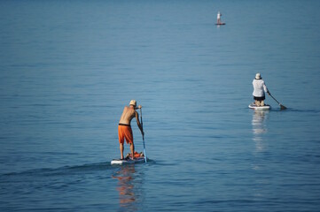 A man standing on a board is rowing with an oar. Sapsurfing. Vacation at the sea.