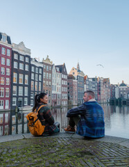 Two friends sit by the peaceful canal, admiring the charming autumn colors of Amsterdam historic...