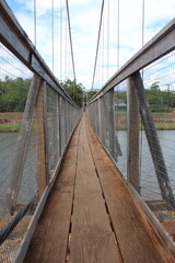Obraz premium Rickety Swinging Wooden Bridge in Kauai, Hawaii (Hanepepe). Three wooden floor boards, windy. Cloudy skies. 
