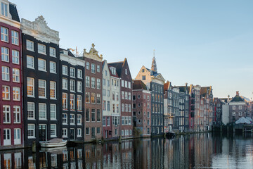 Obraz premium The tranquil canals of Amsterdam shine under autumn's warm hues, with elegant gabled houses lining the water, creating a picturesque view that captures the essence of the city's rich heritage.