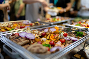 A vibrant buffet display featuring an assortment of grilled meats, colorful vegetables, and garnishments at a bustling event in the evening