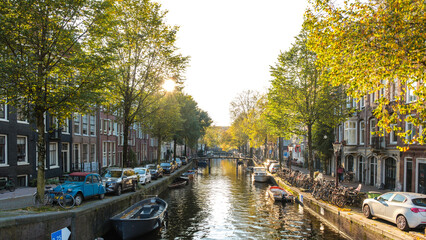 Golden leaves flutter in the crisp autumn breeze as the sun sets over Amsterdam's serene canals. Boats gently float by, reflecting the warm hues of nature and inviting strolls along tree-lined paths.