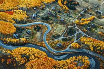 Aerial view of a winding road through an autumn-hued aspen forest in the mountains of Colorado, with small villages
