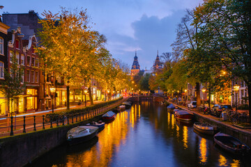 Golden leaves frame the serene canals of Amsterdam as twilight descends, Amsterdam Netherlands canals with Christmas lights during December, canal historical center of Amsterdam at night