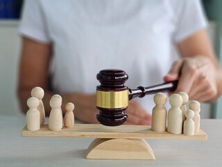 A gavel raised above wooden figurines representing judgment in a courtroom