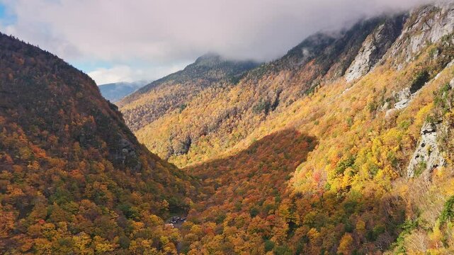 USA, Vermont, Green Mountains, drone flight through Smugglers Notch, a mountain pass with hillsides covered in trees with vibrant fall foliage colors.