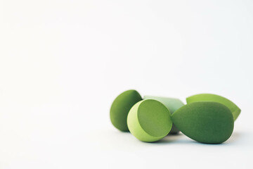 Green makeup sponges on a white background. A minimalist composition showcasing beauty tools for foundation blending, perfect for skincare and cosmetics themes