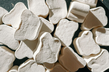 A close-up of fluffy, textured white marshmallows shaped like bones, arranged haphazardly under...