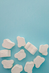 Fluffy white marshmallows in various shapes scattered on a light blue background. Minimalist and playful arrangement ideal for confectionery, dessert, or fun food themes